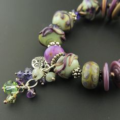 "Like a breath of Spring, you'll love the feel of this handmade lampwork and sterling silver bracelet. The handmade glass beads are combined here with Swarovski crystals and Sterling silver in this one-of-a-kind bracelet. A cluster of Swarovski crystals, and gemstone rondelles including aquamarine and amethyst accents the gorgeous beads in purple, burgundy, celadon, sage and more. A decorative sterling silver butterfly toggle clasp and a dangle of coordinating crystals and gemstones complete the Artisan Czech Glass Beaded Bracelets With Spacer Beads, Unique Bracelet With Faceted Czech Glass Beads, Unique Bracelets With Faceted Czech Glass Beads, Unique Bracelet With Czech Glass Faceted Beads, Lampwork Glass Beads Jewelry, Collage Jewelry, Lampwork Bracelets, Purple Burgundy, Glass Bead Bracelet