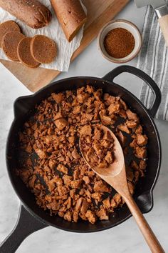 a skillet filled with meat and spices next to some bread on a cutting board