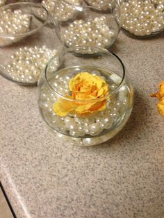 several glass bowls with flowers in them on a counter top, and pearls scattered around the bowl