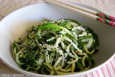 a white bowl filled with noodles and veggies next to chopsticks on a table