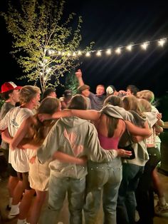 a group of people standing next to each other in front of a tree at night