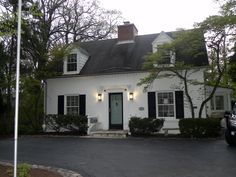 a white house with black shutters and a car parked in front