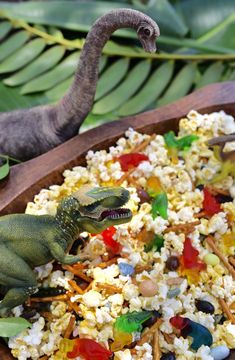 two toy dinosaurs are eating out of a wooden bowl filled with rice and veggies