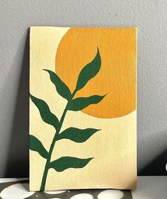 an orange and yellow painting with green leaves in front of it on a white surface