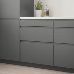 a kitchen with gray cabinets and white counter tops, along with a potted plant