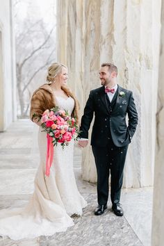 a bride and groom holding hands in front of columns