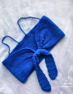 a blue crocheted bag with a tie on it sitting on a white sheet