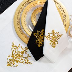 two white and black napkins with gold designs on them sitting next to each other