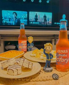 some food and drinks on a table in front of a television set with two cartoon figures