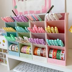 an organized desk with lots of different colored pens and pencils in bins next to a computer keyboard