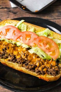 a sandwich with meat, lettuce and tomatoes on it sitting on a black plate