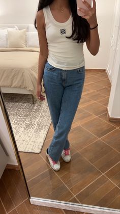 a woman taking a selfie in front of a mirror while wearing jeans and sneakers