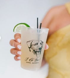 a person holding a drink with a dog on it and a lime wedge in the cup