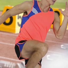 a male athlete in an orange and blue tank top is running on a race track