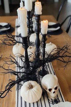 a wooden table topped with white pumpkins and black candlesticks on top of a striped placemat