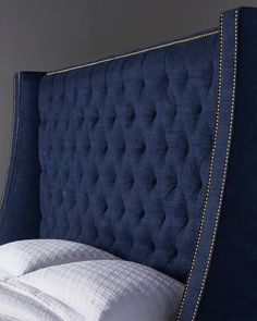 an upholstered headboard on a bed with white sheets and blue linens