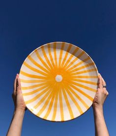 two hands holding up a yellow and white plate in the air against a blue sky