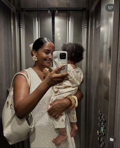 a woman holding a baby taking a selfie in a bathroom mirror with her cell phone