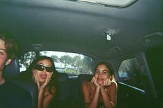 three people sitting in the back seat of a car with their hands on their mouths