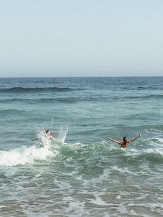 two people swimming in the ocean with their arms spread out and one person is falling off his surfboard