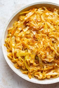 a white bowl filled with cabbage and meat on top of a marble countertop next to a fork