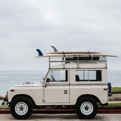 a white truck with a surfboard on top of it's roof and the ocean in the background