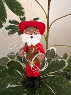 a small figurine with a red hat and white beard standing in front of a green plant