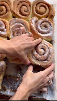 two hands grabbing doughnuts out of a baking pan with cinnamon rolls in the background