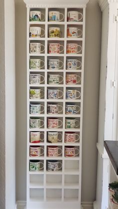 a white bookcase filled with coffee mugs in a kitchen next to a wall