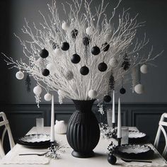 black and white christmas decorations in a vase on a dining room table with candlesticks