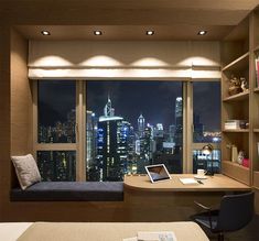 a bedroom with a desk, bookshelf and window overlooking the city at night