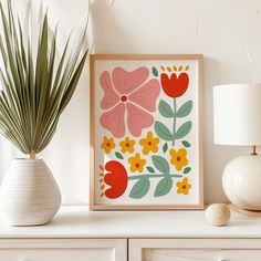 a white dresser topped with a vase filled with flowers next to a framed art print