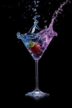 a martini glass filled with water and colorful fruit splashing out of it's side