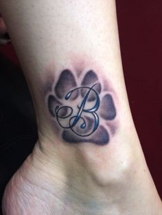 a tattoo on the foot of a person with a dog paw and initial letter b