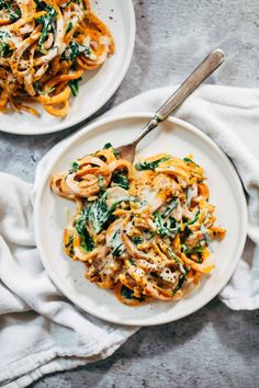 two plates of pasta with chicken and spinach on them, one has a fork in it