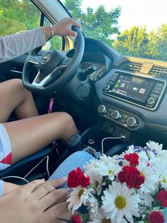 a woman sitting in the driver's seat of a car next to a bouquet of flowers