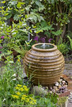 a water fountain in the middle of a garden with lots of plants and flowers around it