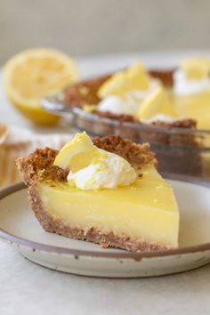 a slice of lemon pie on a plate with the rest of the pie in the background