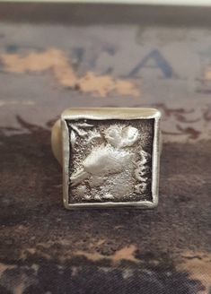 a square silver ring with an image of a bird on it's back side