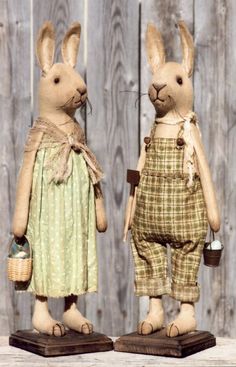 two stuffed rabbits dressed in clothes standing next to each other on top of wooden boards