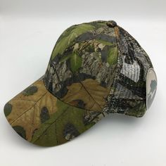 a camo baseball cap with leaves on the front and back side, sitting on a white surface