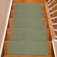 a set of stairs with green carpet and wooden handrails in a home setting