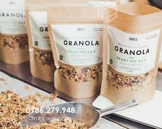 some granola is sitting on a table next to spoons and bags of granola