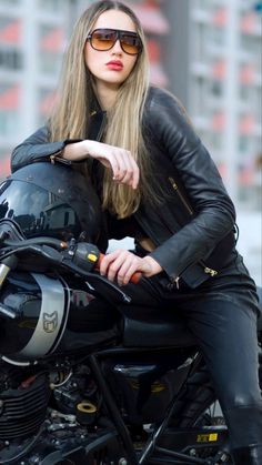 a woman sitting on the back of a motorcycle wearing black leather pants and sunglasses,