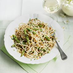 a white plate topped with pasta and asparagus next to a glass of wine