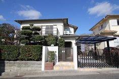 a white house with a black gate and some bushes on the side of the street