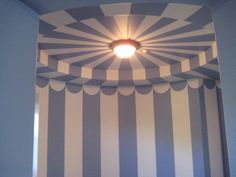 a bathroom with blue and white stripes on the wall next to a round light fixture