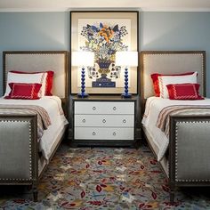 two beds in a room with blue walls and carpeted flooring, one has red pillows on it