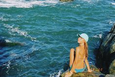 a woman sitting on top of a rock next to the ocean with her eyes closed