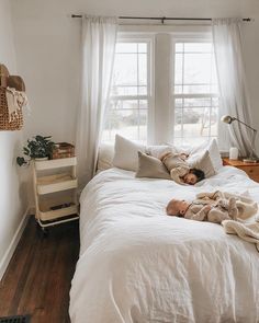 a woman laying on top of a white bed in a bedroom next to a window